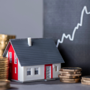 Photo d'illustration montrant une maison miniature, des tas de pièces illustrant la notion de tarif et au fond, une courbe ascendante illustrant la montée du prix de l'immobilier à Chambéry au m²