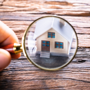 Photo d'une maison miniature scrutée à la loupe pour illustrer l'article "préparer une visite immobilière" de Baobab Immobilier